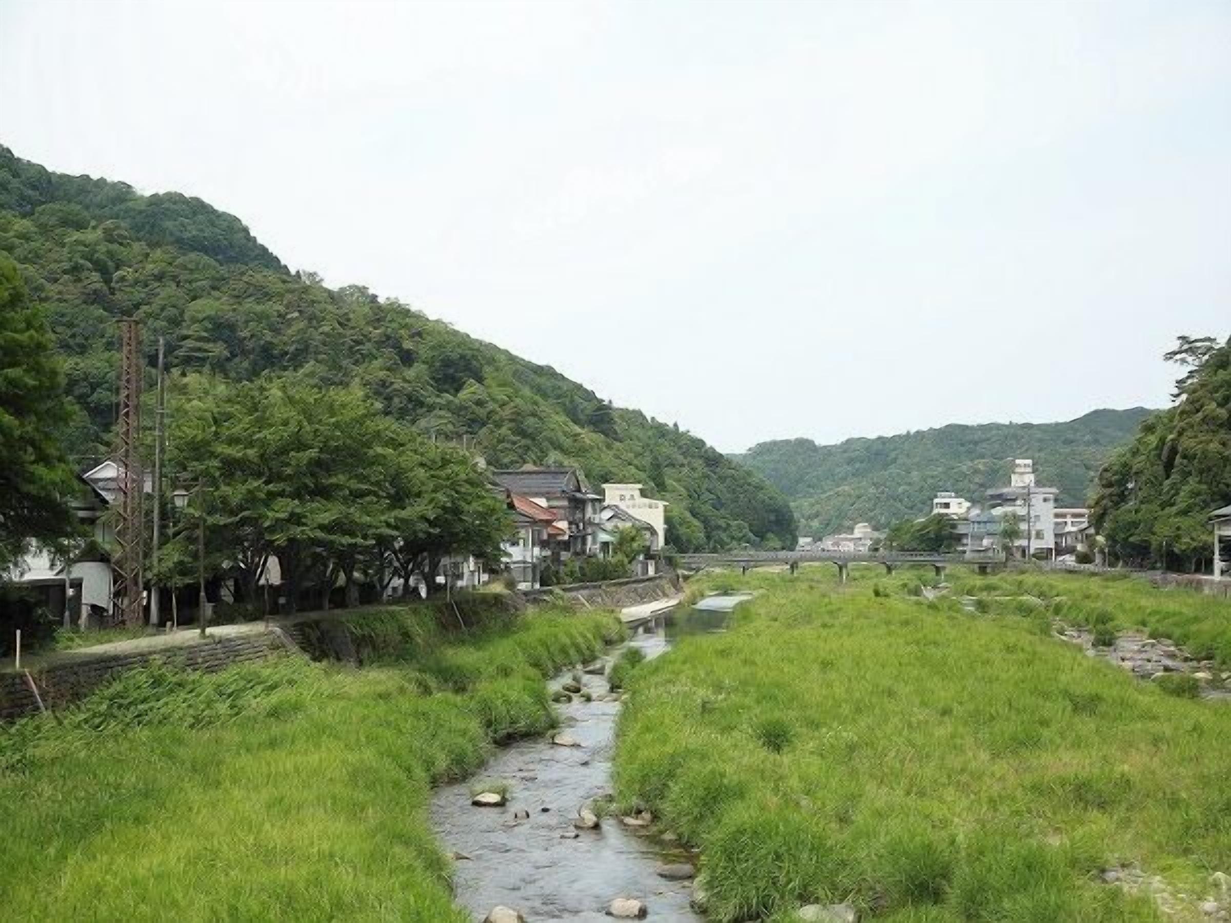 Un paysage rural avec un ruisseau, des maisons et un pont.