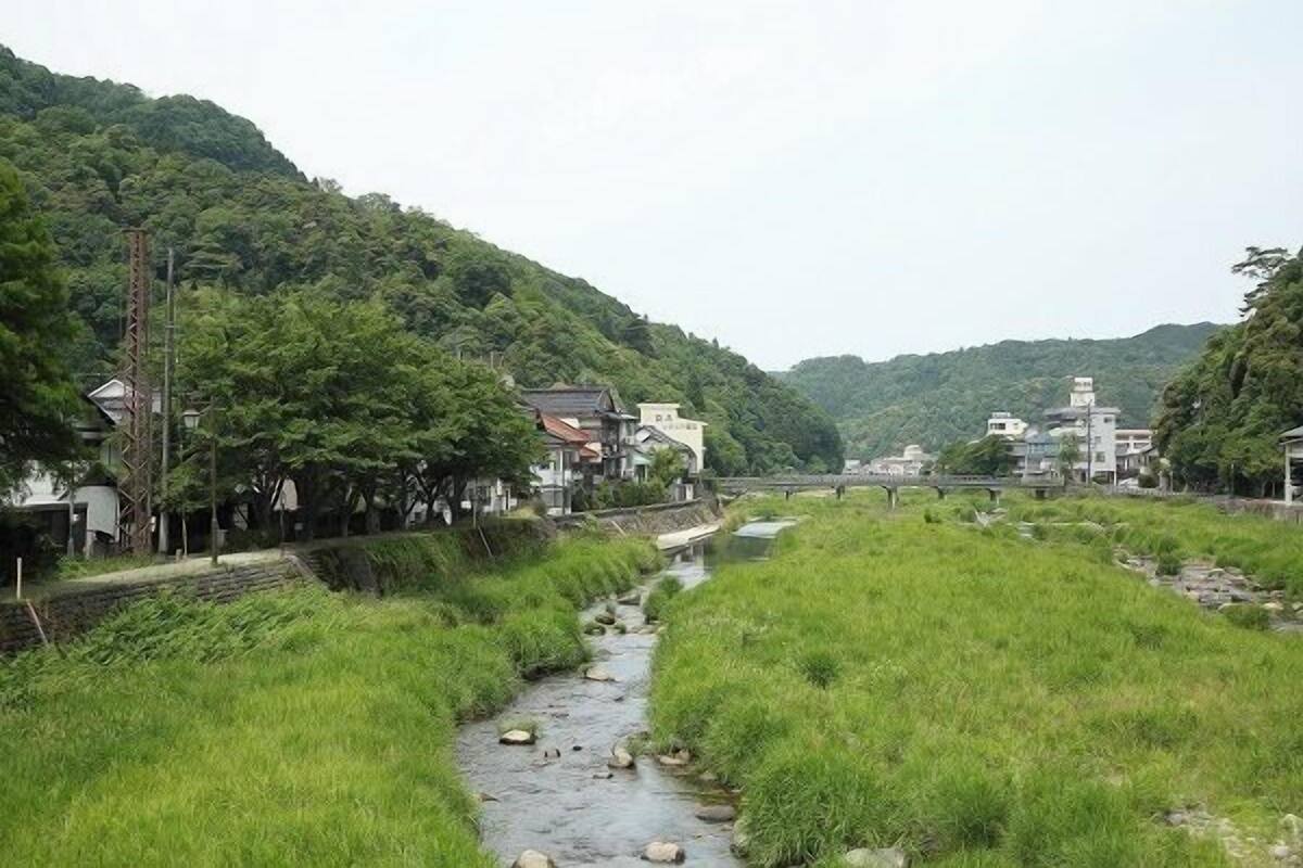 A rural landscape with a stream, houses, and a bridge.