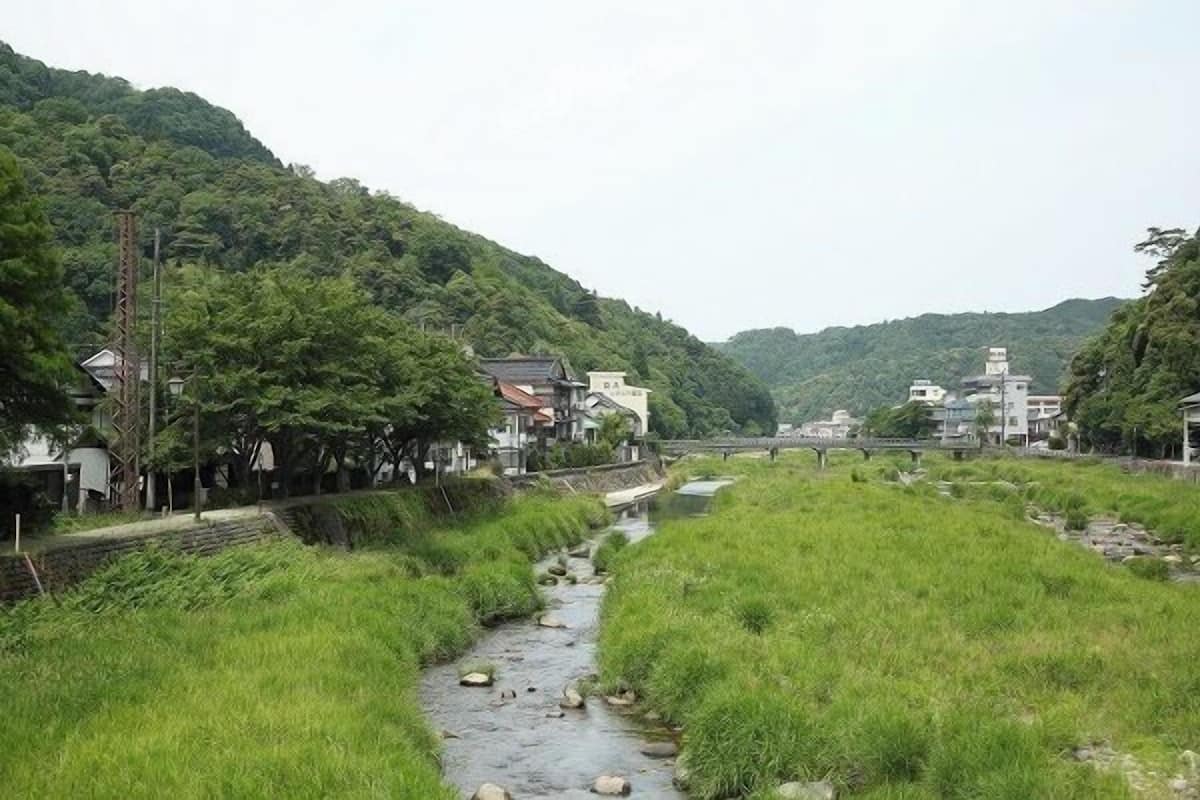 Un paysage rural avec un ruisseau, des maisons et un pont.
