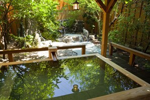 A tranquil garden with a wooden deck, a koi pond, and a waterfall.
