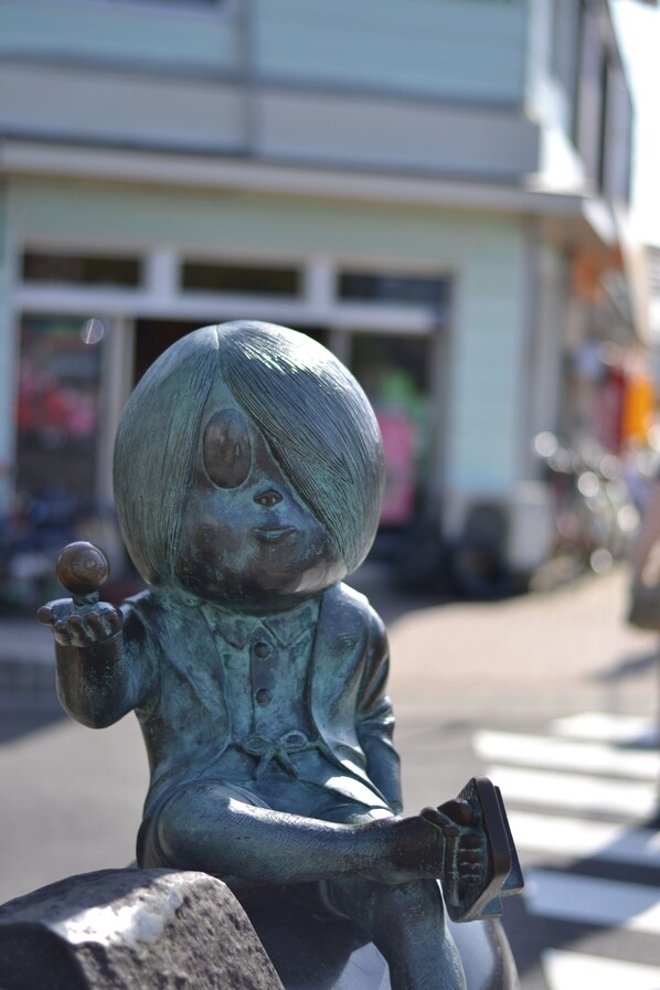 A bronze statue of a child holding a ball and a book, placed on a stone pedestal.