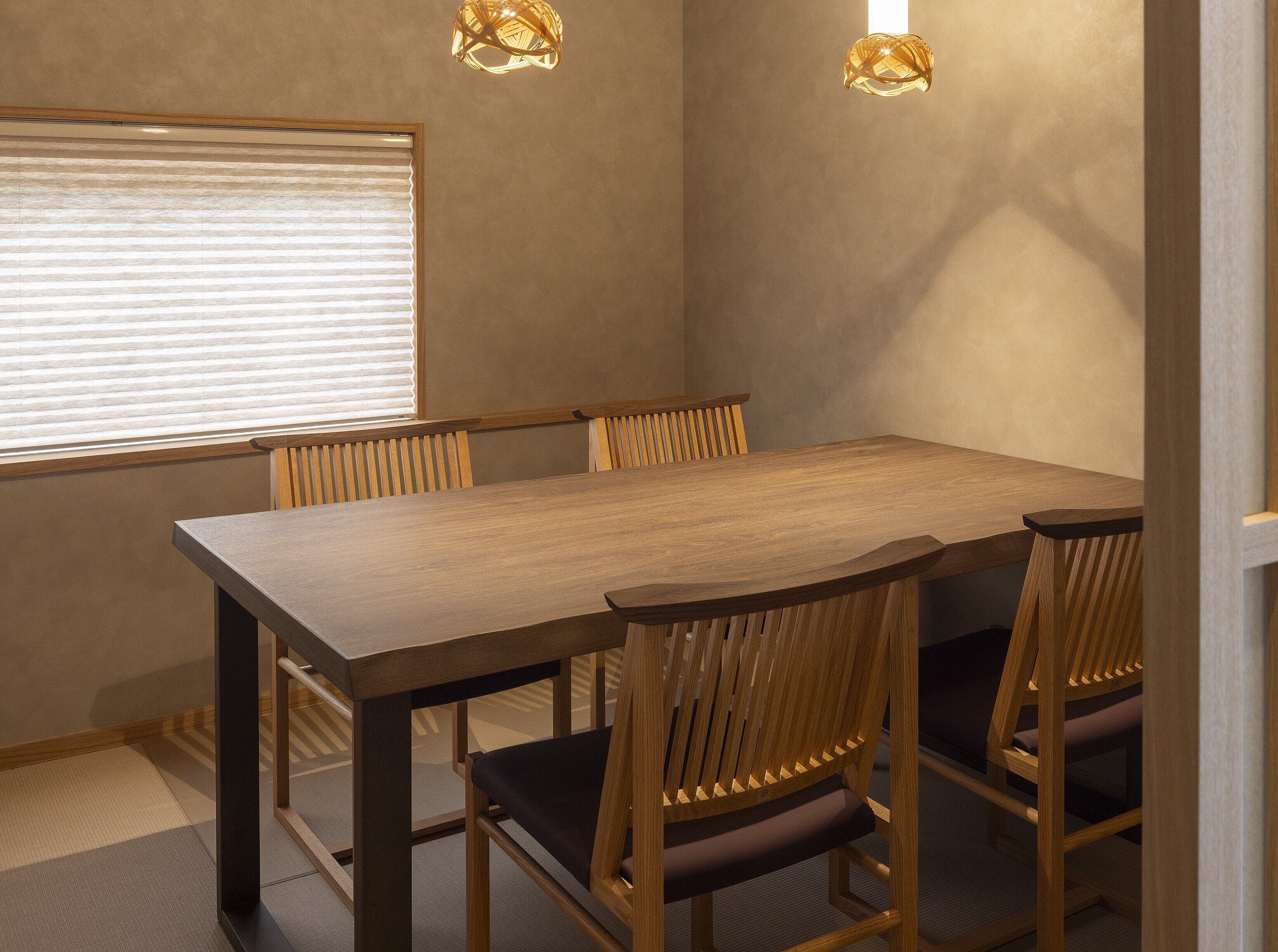 A conference room with a wooden table and chairs, a window with blinds, and two wall-mounted lamps.