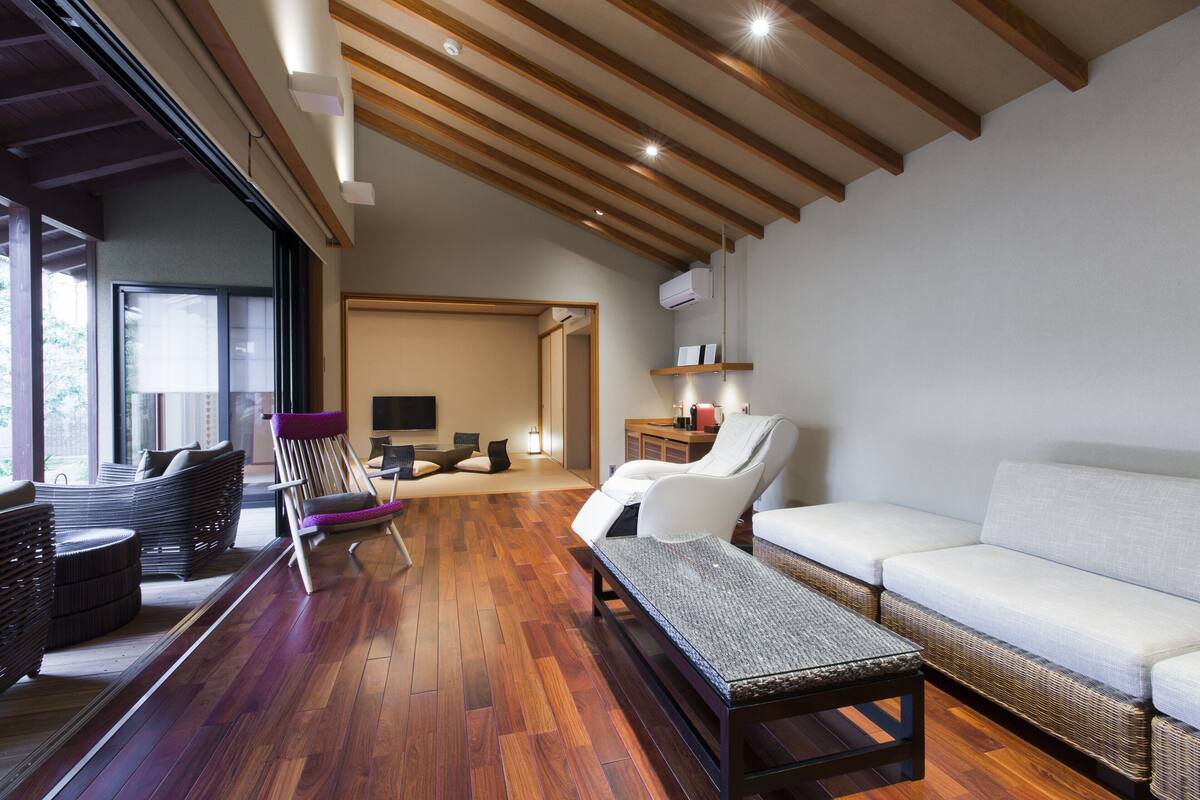 A modern living room with a wooden floor, a white sofa, a wicker chair, and a flat-screen TV.