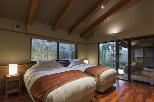 A bedroom with a large bed, wooden beams, a sliding glass door, and a nightstand with a lamp. - Kizukuri no Yado Hashizuya (Misasa)