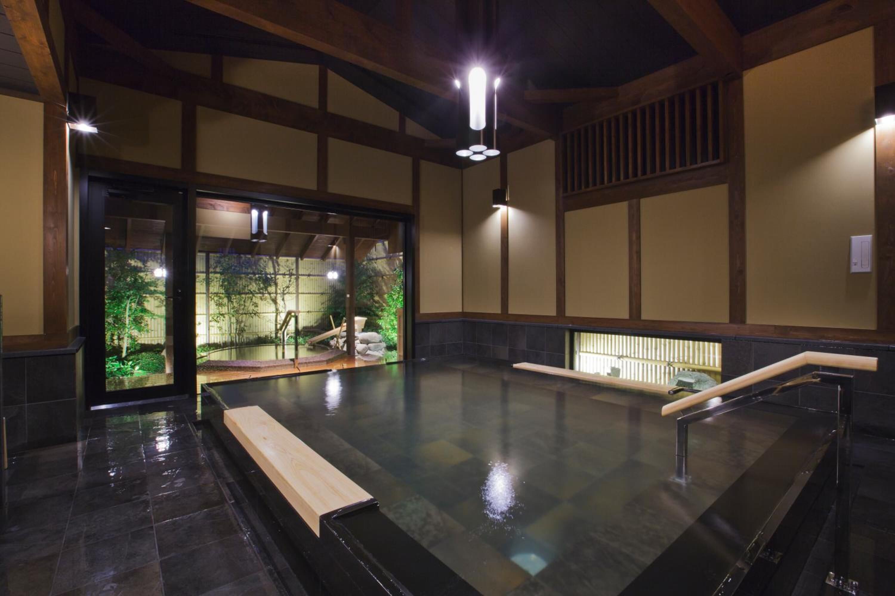 Un onsen japonés tradicional con un banco de madera, una plataforma de piedra y vistas a un jardín a través de puertas correderas.