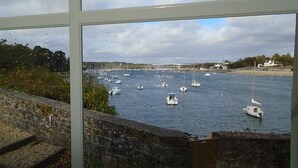 Vista de un puerto con varios barcos, un muro de piedra y una costa lejana con edificios.