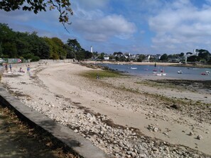 A beach with a rocky shoreline, a lighthouse in the distance, and a few boats on the water.