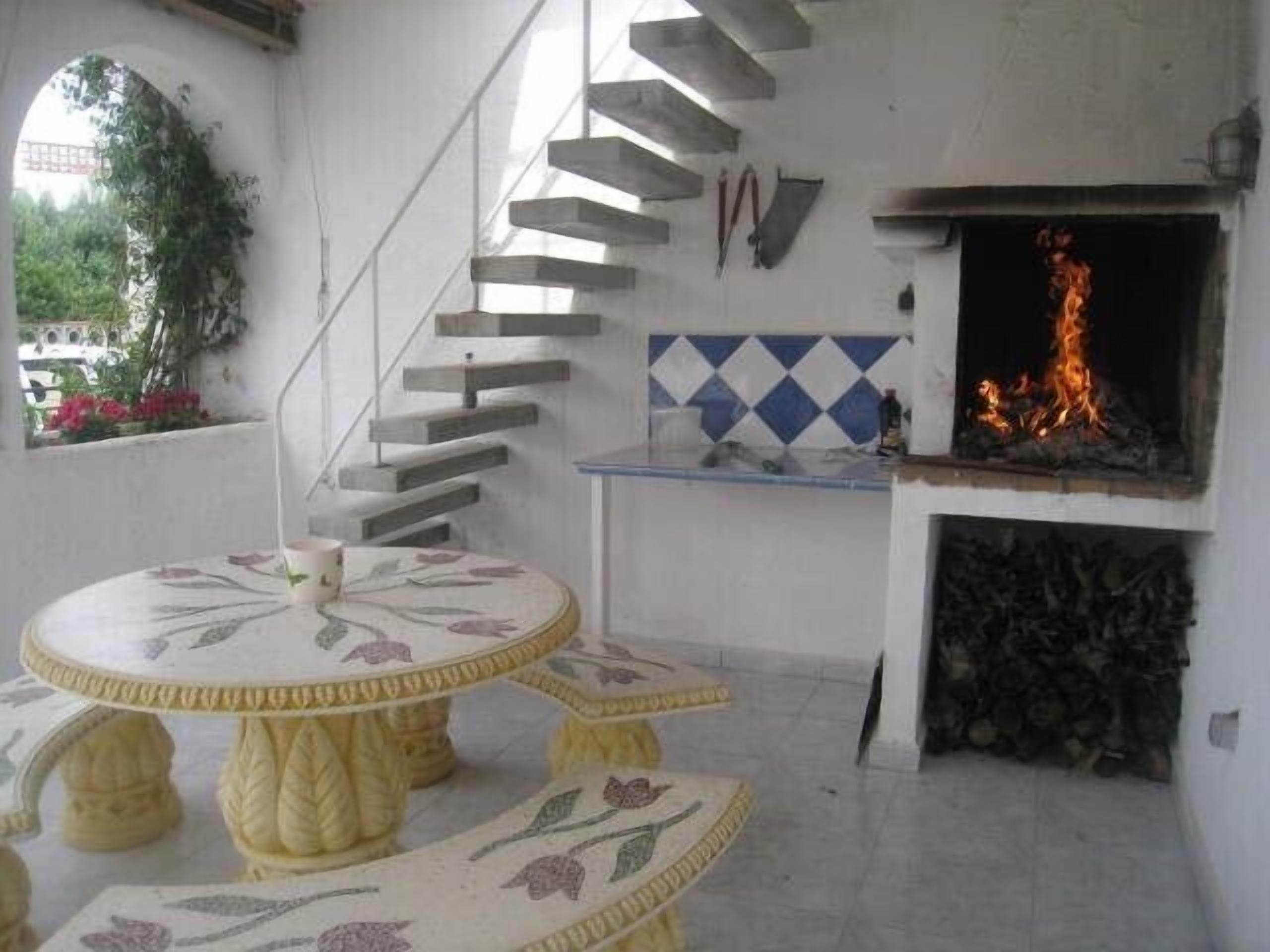 A dining area with a round table and matching stools, a fireplace, and a staircase.