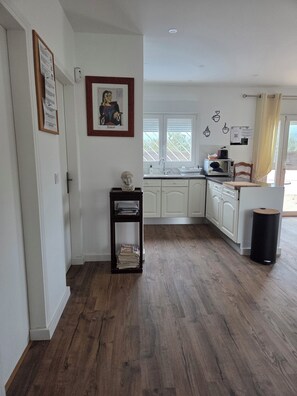 A modern kitchen with white cabinets, a wooden floor, a microwave, and a trash bin.