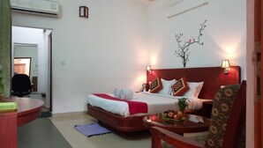 A hotel room with a bed, a desk, a chair, and a small table with fruit. - Vythiri Greens Resort (Vythiri)
