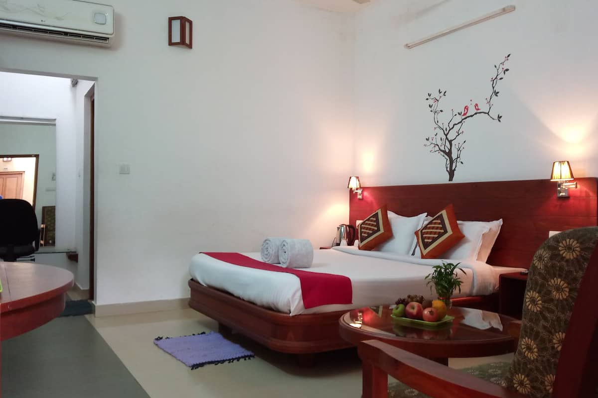 A hotel room with a bed, a desk, a chair, and a small table with fruit.