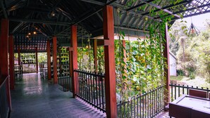 A covered outdoor area with a tiled floor, wooden pillars, and a black metal railing. - Vythiri Greens Resort (Vythiri)