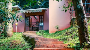 A set of outdoor concrete steps leading to a building with a pink facade and a covered entrance. - Vythiri Greens Resort (Vythiri)