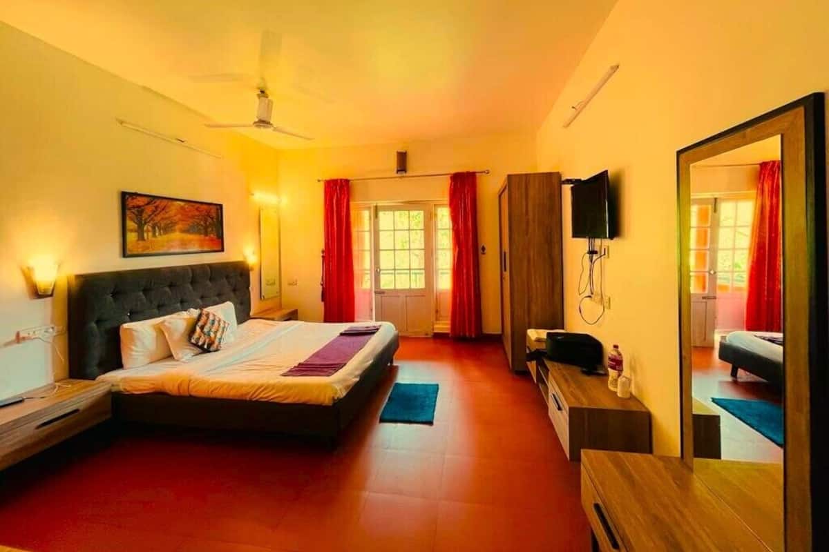 A bedroom with a bed, a desk, a mirror, and a television.