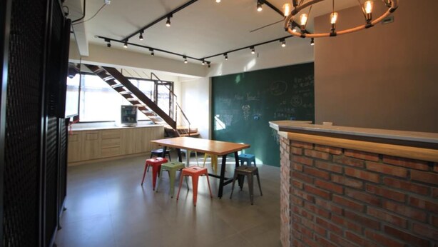 A modern interior with a staircase, a chalkboard wall, and a wooden table with stools. - Box Inn Jiufen - Hostel (New Taipei City)
