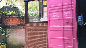 A pink shipping container with weight and capacity labels, a brick wall, and a window with a view of greenery. - Box Inn Jiufen - Hostel (New Taipei City)