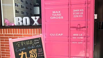 Um contentor rosa com indicações de limite de peso e um quadro negro a anunciar um hostel cápsula.