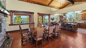 Un comedor amplio con una gran mesa de madera y seis sillas tapizadas, una chimenea de piedra y vistas a un lago a través de amplios ventanales.