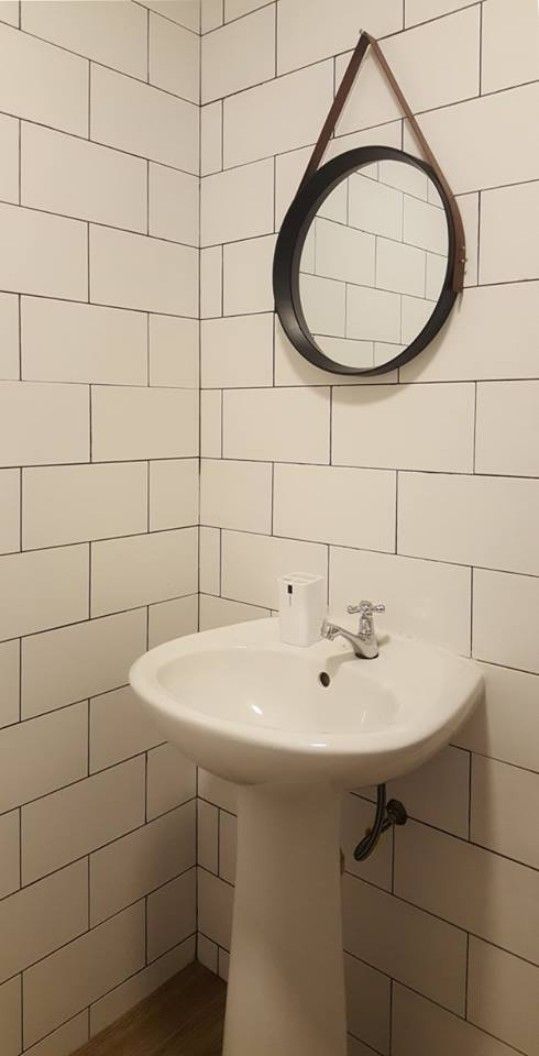Ein Badezimmer mit weiß gefliesten Wänden, einem weißen Standwaschbecken und einem runden Spiegel mit braunem Rahmen.