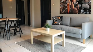 A modern living room with a grey sofa, a coffee table, and a cityscape painting on the wall. - Elopura Vacation Apartment (Kota Kinabalu)