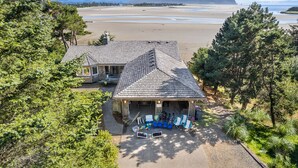 Een huis met schuin dak, een veranda met buitenmeubilair, en uitzicht op een strand en bergen op de achtergrond.
