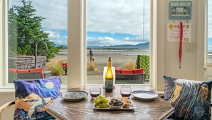 Een tafel met een fles wijn, glazen en een schaal druiven en olijven, met uitzicht op een strand.