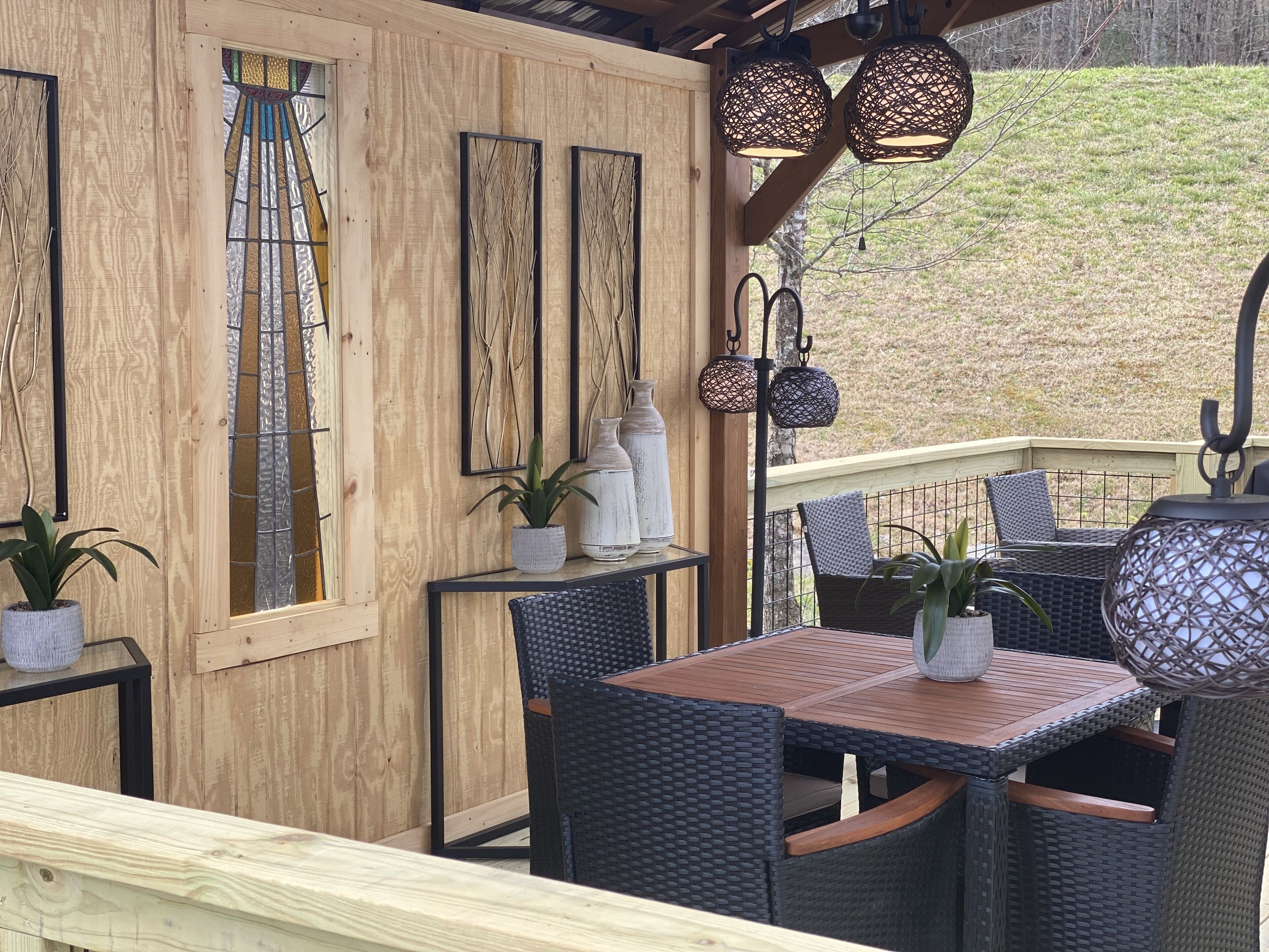 Une terrasse en bois, meublée de meubles en osier, avec une porte vitrée et un éclairage décoratif.