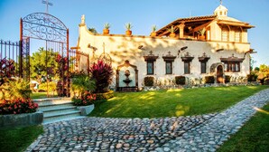 Un edificio con un camino de piedra que conduce a una puerta, rodeado de jardines cuidados y un cielo despejado.