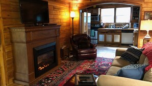 Una sala de estar acogedora con chimenea, sillón de cuero y sofá con cojines estampados.