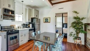 Una cocina con pisos de madera, gabinetes blancos, una mesa de comedor con sillas y una planta grande en maceta.
