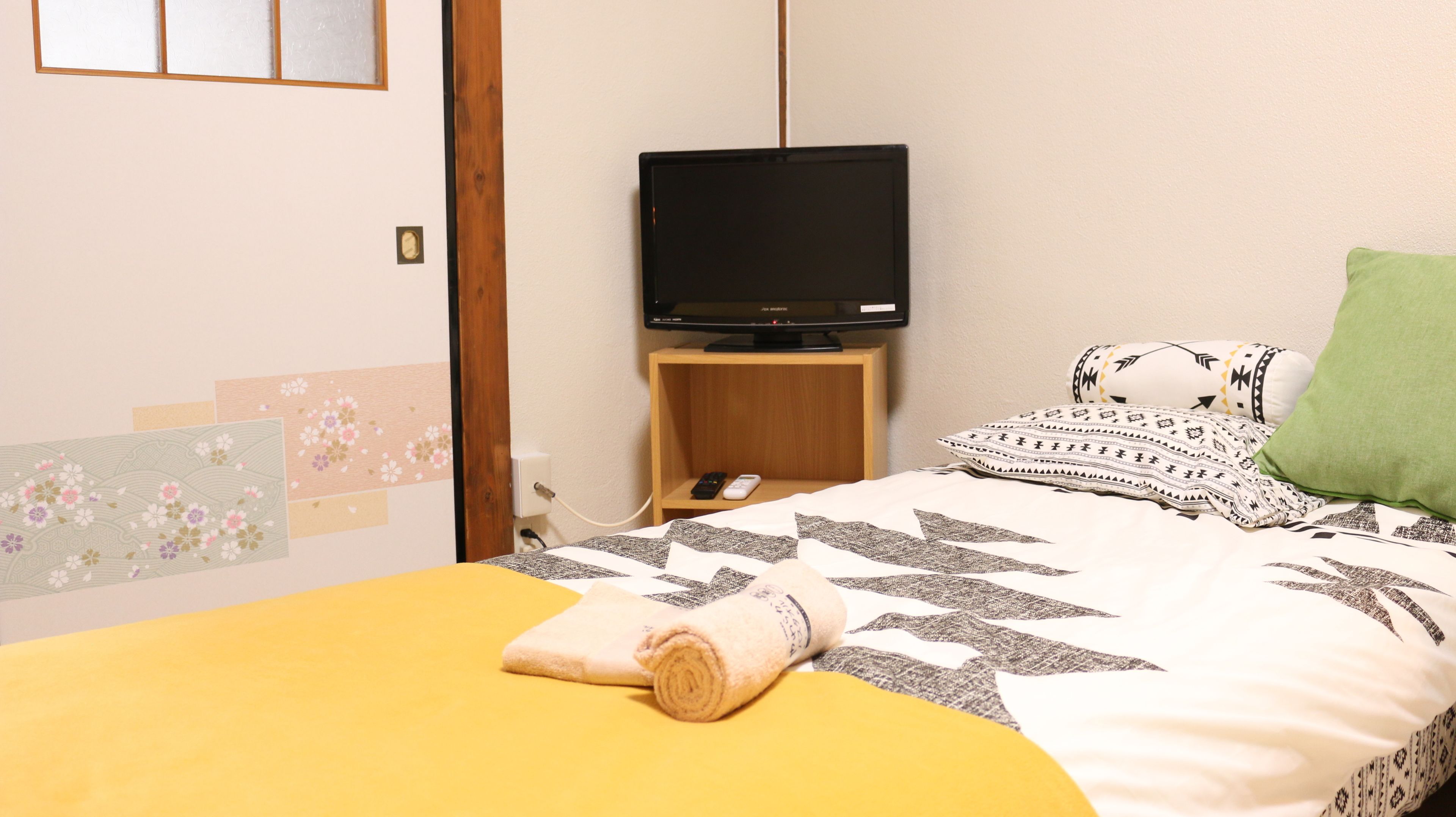 A hotel room with a bed, a television on a wooden stand, a remote control, and decorative pillows.