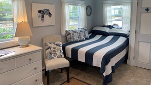 A bedroom with a bed, a chair, a dresser, and a window with curtains.