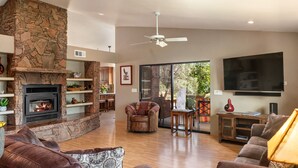 A spacious living room with a stone fireplace, leather sofas, a ceiling fan, and a large TV. - Pet Friendly
Hike, Bike, Enjoy! (Sedona)