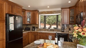 A kitchen with wooden cabinets, granite countertops, a black refrigerator, and a breakfast bar with cheese, crackers, and a wine bottle. - Pet Friendly
Hike, Bike, Enjoy! (Sedona)