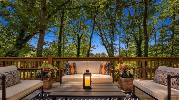 Une terrasse avec un canapé, deux petites tables d’appoint, une lanterne et des plantes en pot.