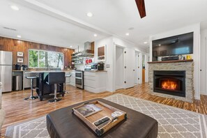 Eine moderne Küche mit Kamin aus Stein, einer Essecke mit Barhocker und einem Wohnzimmer mit Kamin.