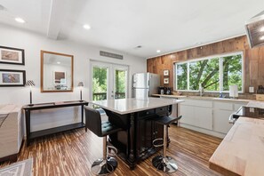 A modern kitchen with a central island, bar stools, and a view of the outdoors.