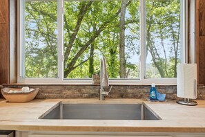 Eine Küche mit großem Fenster, einem Edelstahl-Spülbecken, einer Holzschüssel und einer Flasche Geschirrspülmittel.