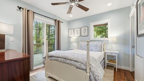 Une chambre à coucher avec un lit, des tables de chevet, un ventilateur de plafond et une fenêtre donnant sur des arbres.