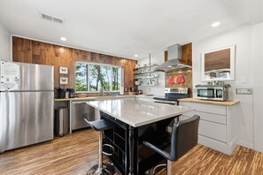 A modern kitchen with a central island, stainless steel appliances, wooden paneling, and a view of trees.
