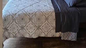 A bedroom with a wooden ceiling, a ceiling fan, a bed with patterned bedding, and butterfly wall art.