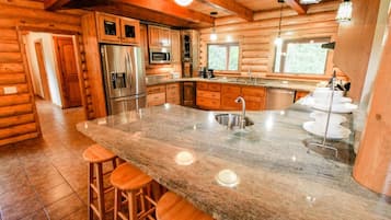 A log cabin kitchen with a granite island, stainless steel appliances, and wooden bar stools.