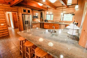 Cucina di una baita in legno con isola in granito, elettrodomestici in acciaio inossidabile e sgabelli da bar in legno.