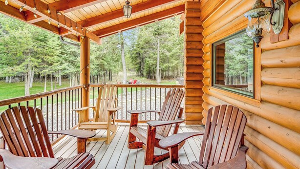 En træterrasse med Adirondack-stole og et bord, med udsigt over et skovområde.