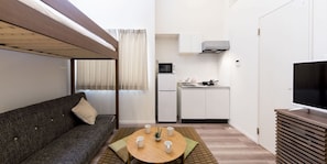 A compact living space with a sofa, a small dining table, a kitchenette, and a TV. - Trip Pod Tojin-Machi A (Fukuoka)