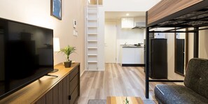 A compact living space with a TV, a small plant, a sofa, a kitchen area, and a ladder. - Trip Pod Tojin-Machi A (Fukuoka)