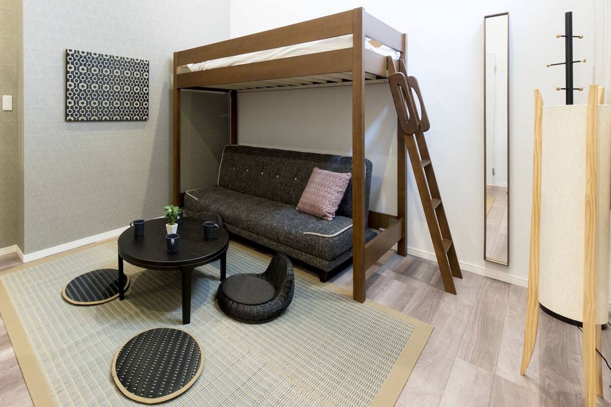 A room with a bunk bed, a sofa, a small table, and a chair.