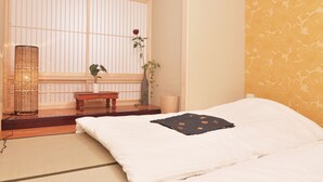 A traditional Japanese-style room with tatami flooring, a shoji screen, a wooden table, a vase with a single red rose, and a bed with a black patterned pillow. - Shirakabanoyado-fuka (Osaka)