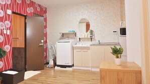 A compact hotel room with a kitchenette, a wooden door, a vacuum cleaner, a potted plant, and a mirror. - Shirakabanoyado-fuka (Osaka)