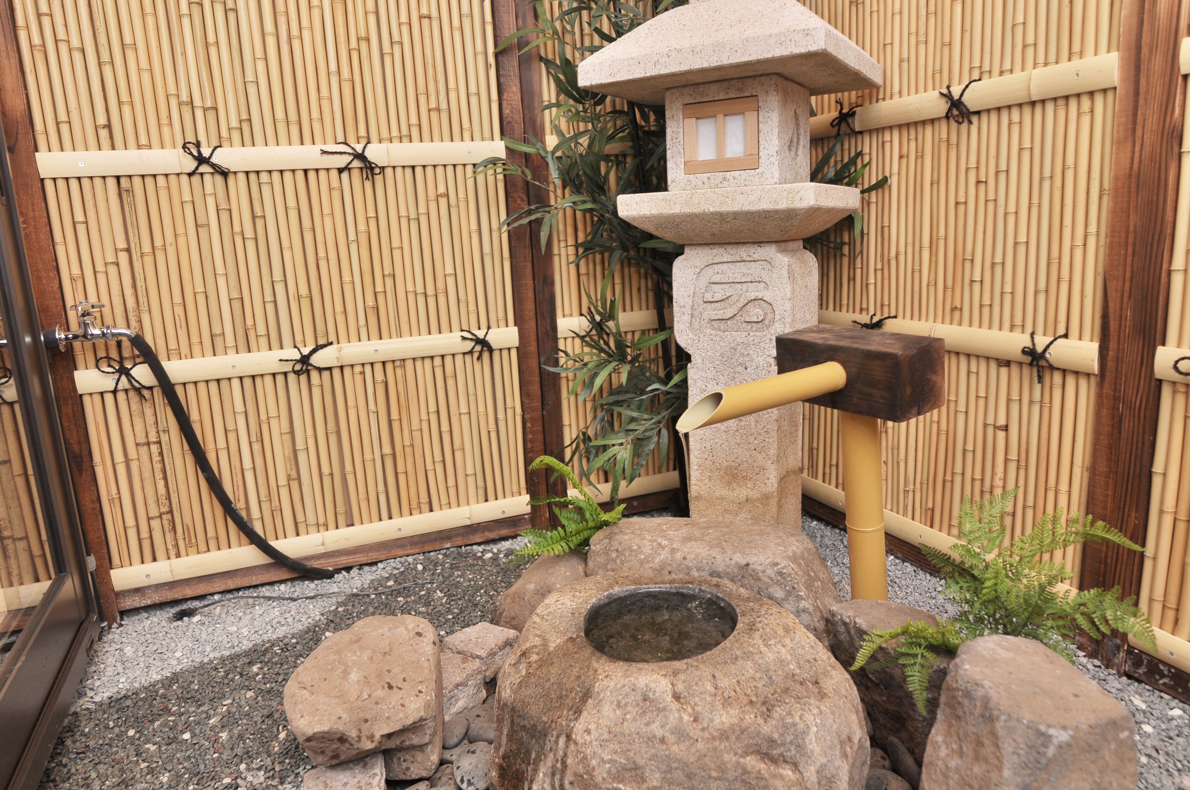 Un jardín japonés tradicional con un farol de piedra, una cerca de bambú y un pequeño estanque.